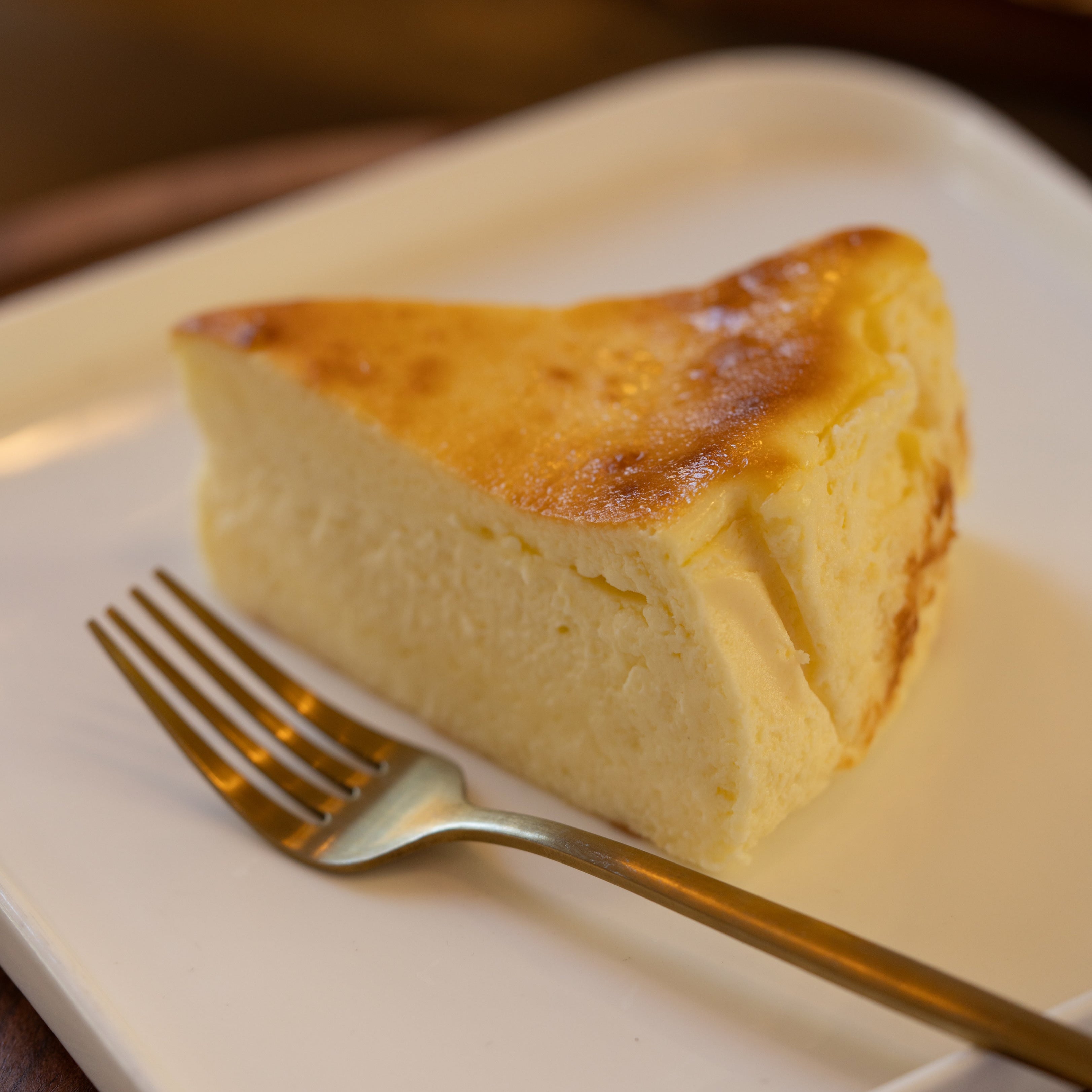 Slice of cheesecake on a white plate with a fork, blurred background