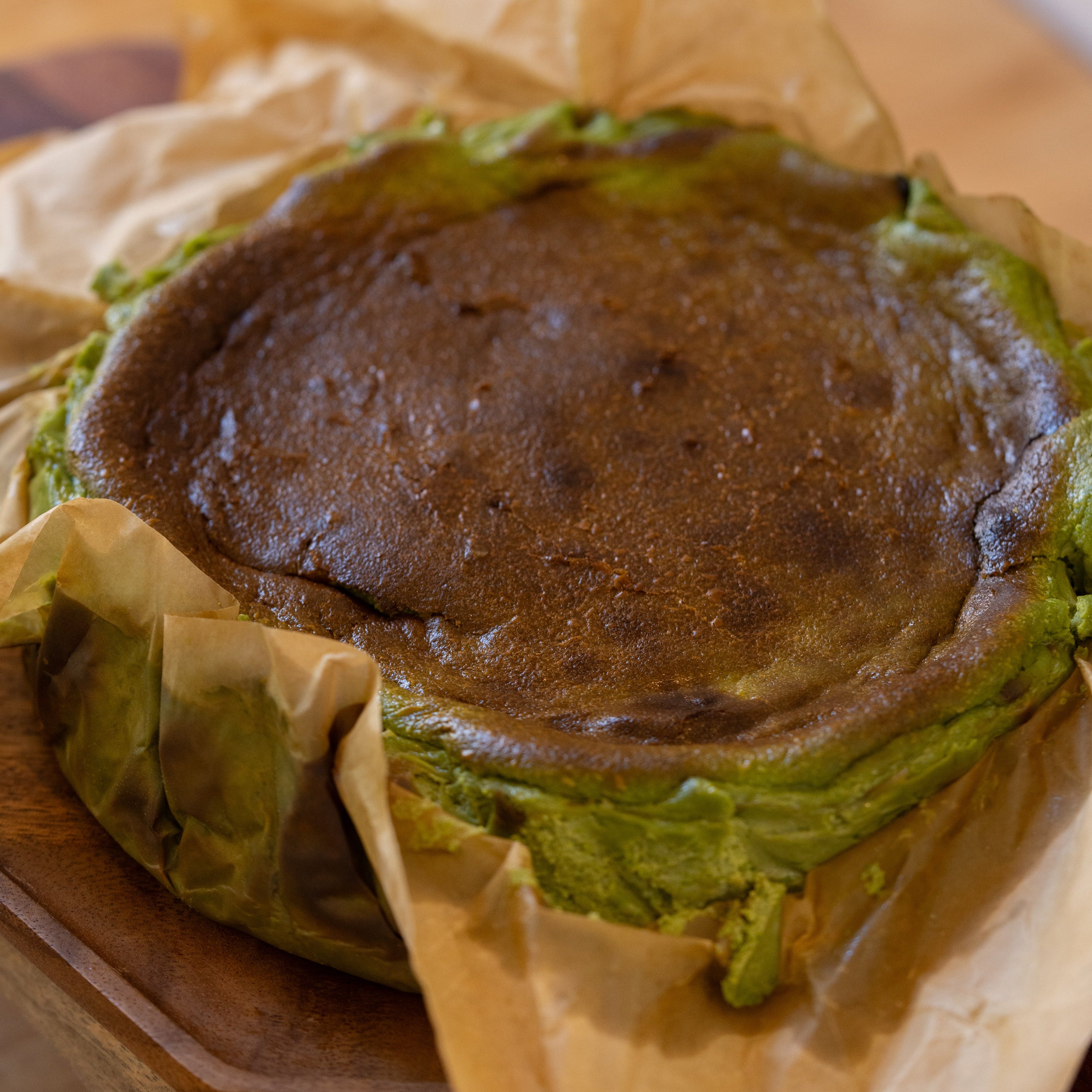 matcha basque cheesecake wrapped in brown paper on a wooden surface
