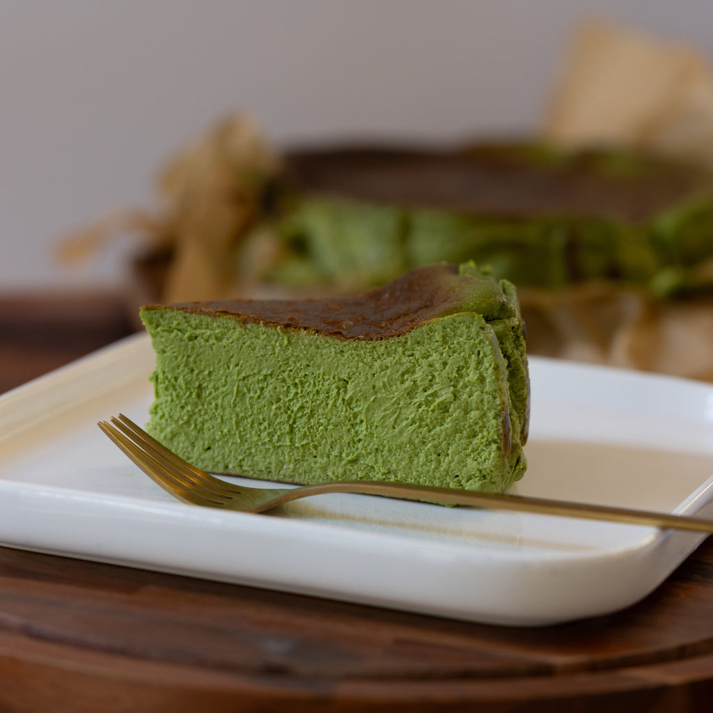 Slice of green tea cheesecake on a white plate with a fork, blurred background