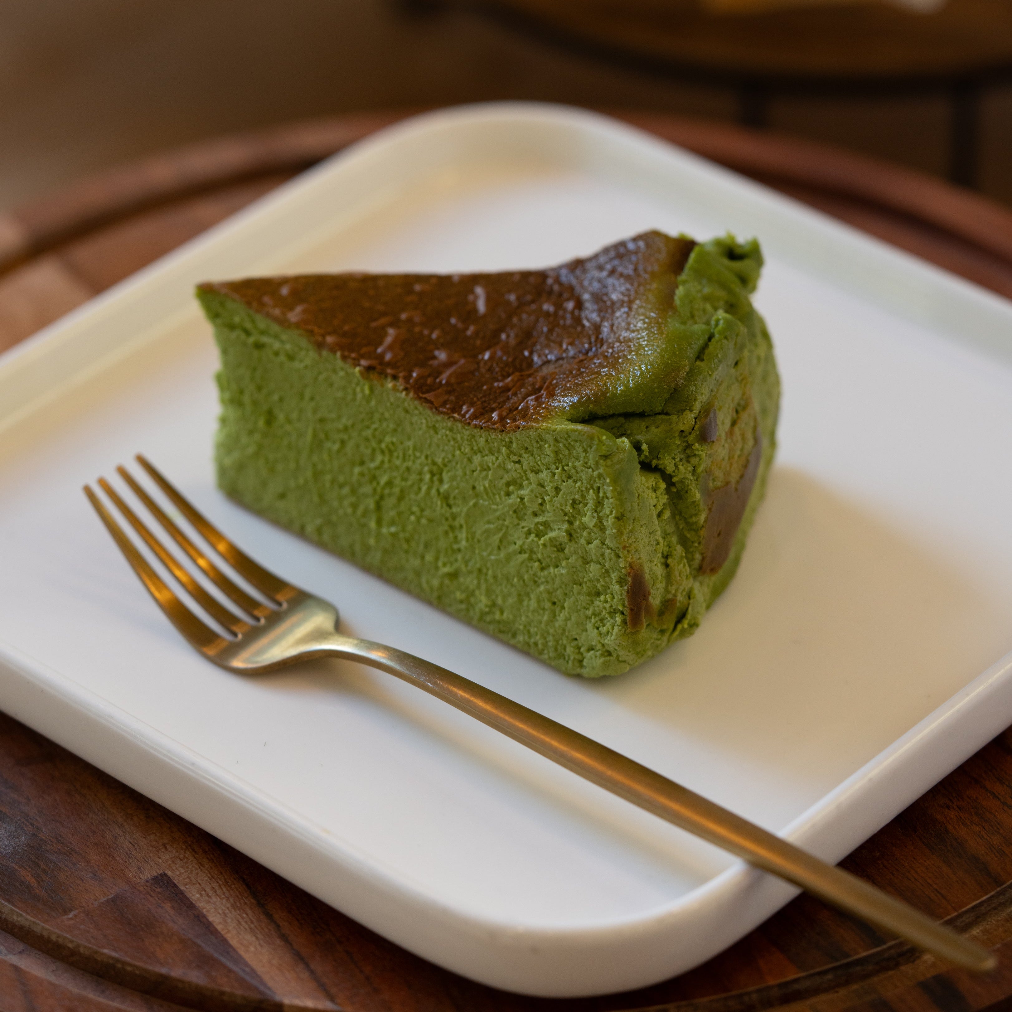 Slice of green tea cake on a white plate with a gold fork