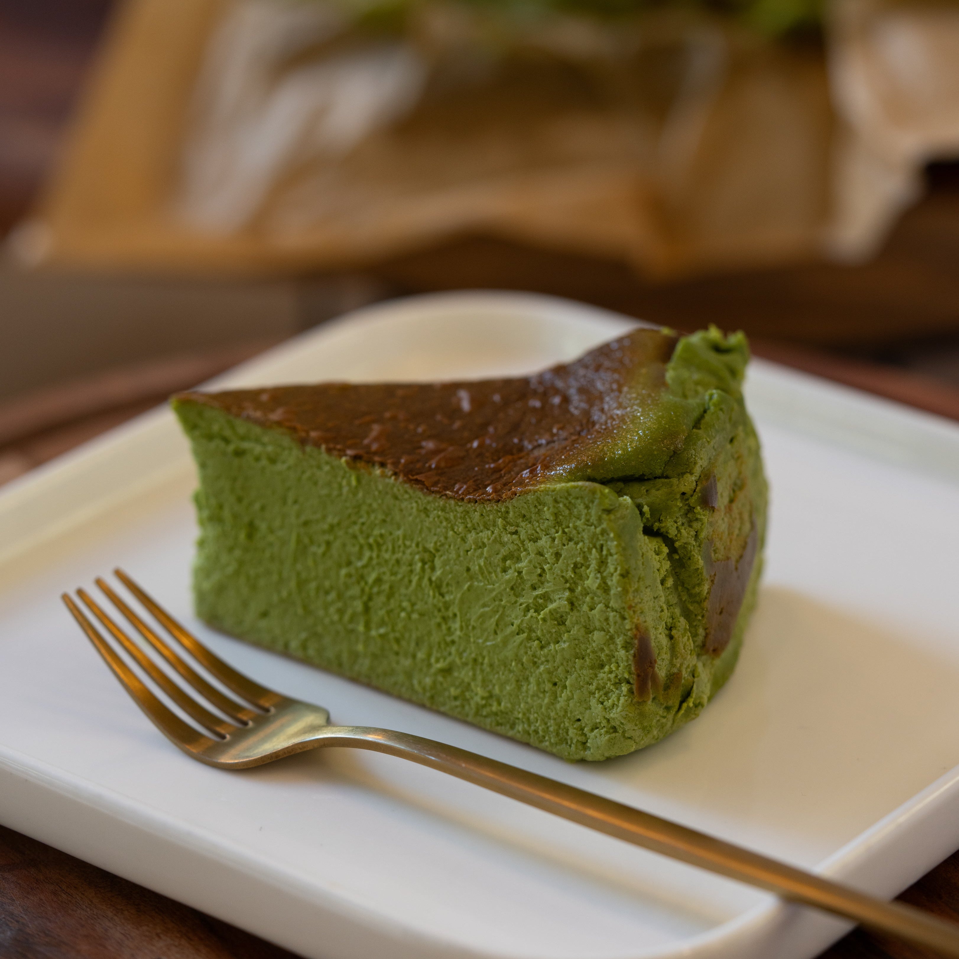 Slice of green cake on a white plate with a gold fork, blurred background