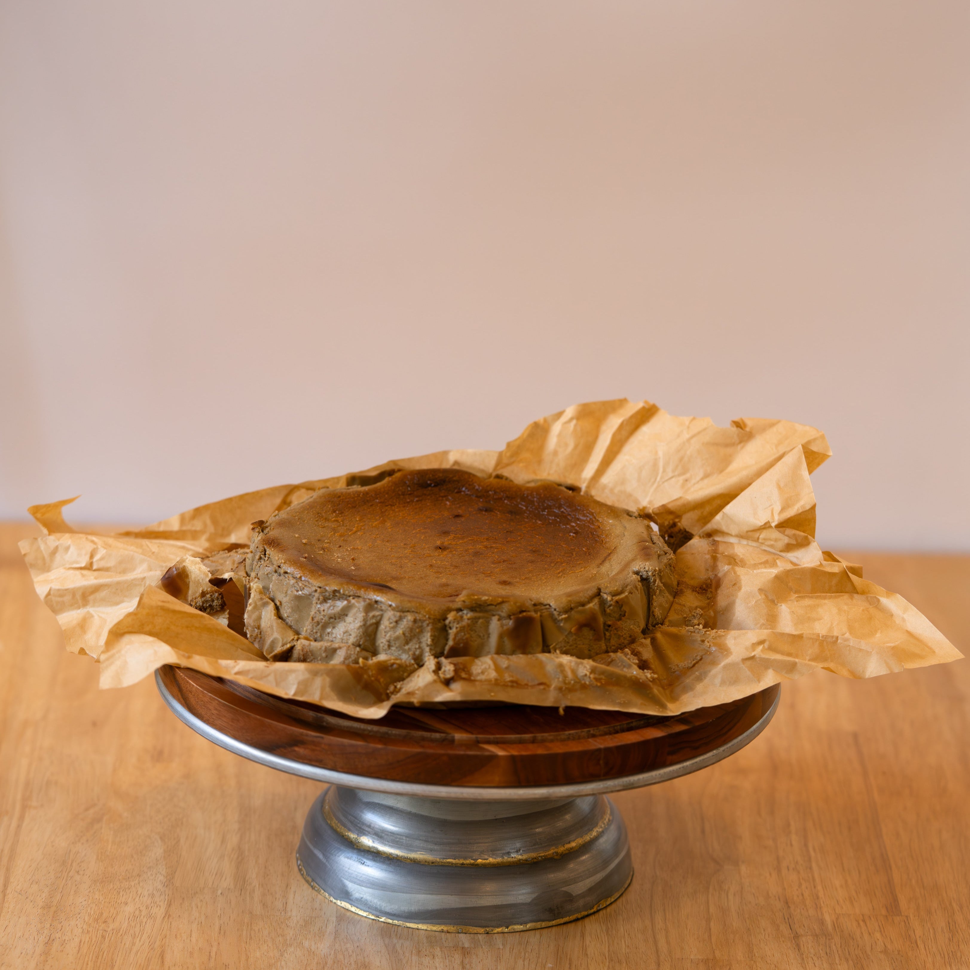 Wooden cake on a metal stand with brown paper wrapping on a wooden surface.