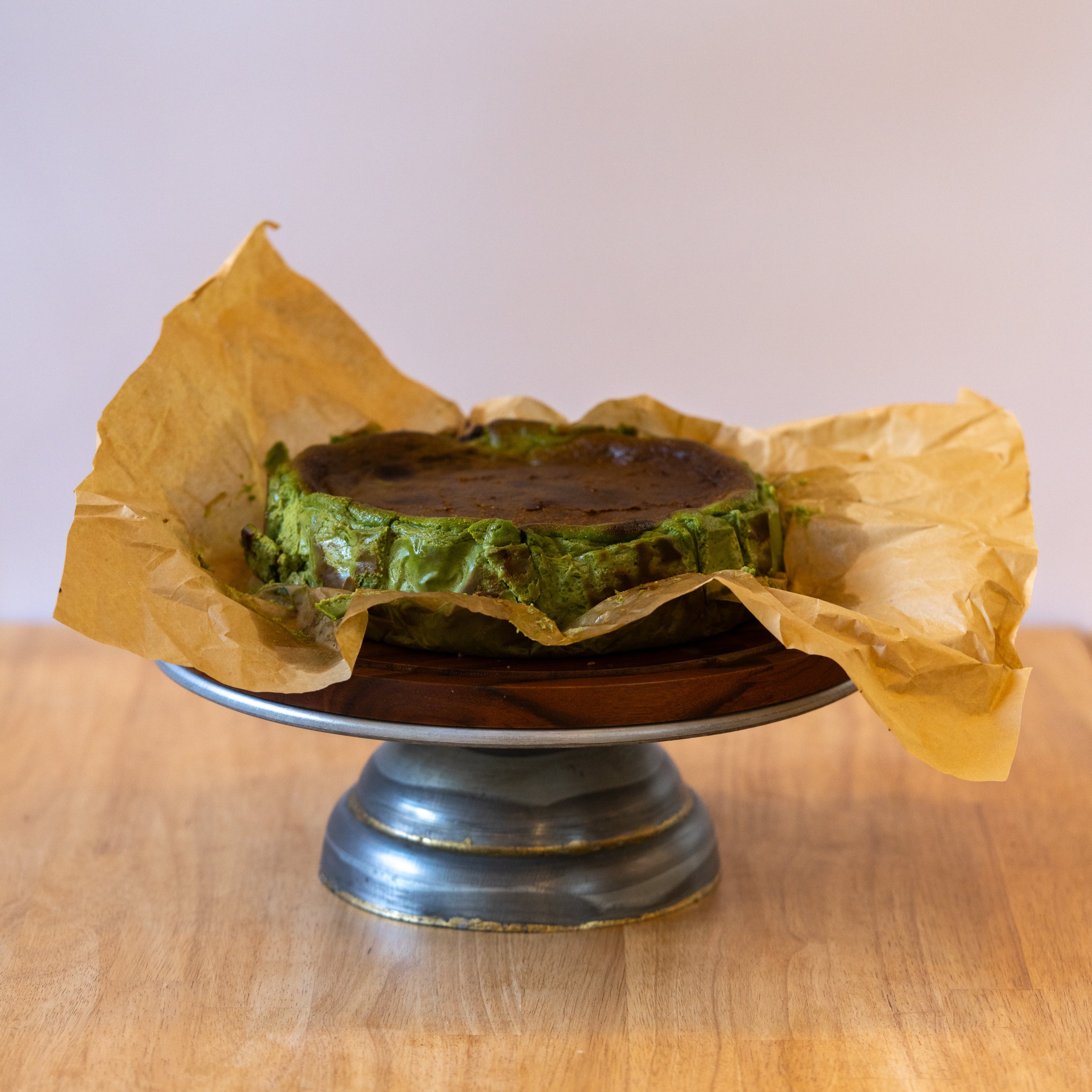 Green cake wrapped in yellow paper on a wooden stand with a light background